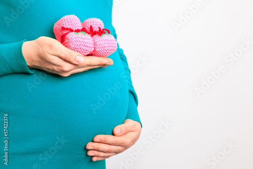 Photo: Pregnant woman holding pink baby shoes on her belly Pregnant woman holding pink baby shoes on her belly