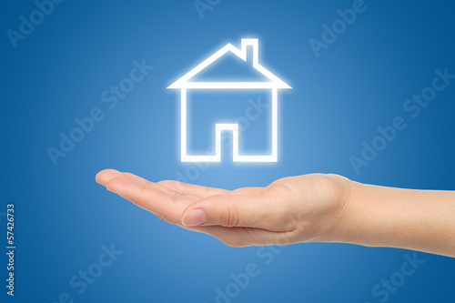 Photo: Virtual house with woman hand on blue background . Virtual house with woman hand on blue background .