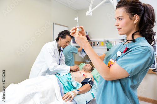 Photo: Nurse Preparing Injection While Doctor And Colleague Examining P Nurse Preparing Injection While Doctor And Colleague Examining P