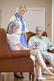 Photo: Smiling home caregiver talking to senior couple with digital tablets in armchairs Smiling home caregiver talking to senior couple with digital tablets in armchairs