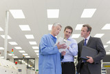 Photo: Engineer and businessmen looking down at clipboard in hi-tech electronics factory Engineer and businessmen looking down at clipboard in hi-tech electronics factory