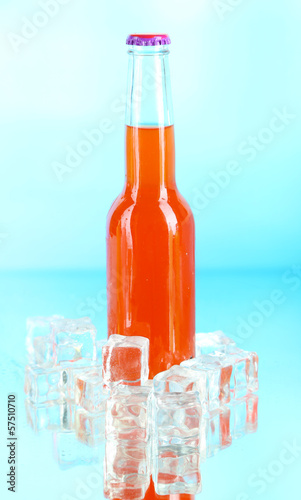Photo: Drink in glass bottle with ice cubes on blue background Drink in glass bottle with ice cubes on blue background