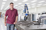 Photo: Portrait of smiling technician standing next to measurement probe in steel bearing manufacturing plant Portrait of smiling technician standing next to measurement probe in steel bearing manufacturing plant