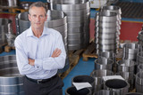 Photo: Portrait of serious Businessman standing among steel roller bearings in manufacturing plant Portrait of serious Businessman standing among steel roller bearings in manufacturing plant