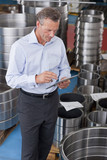 Photo : Businessman using digital tablet among steel roller bearings in manufacturing plant Businessman using digital tablet among steel roller bearings in manufacturing plant