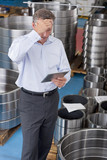 Photo : Businessman with head in hands using digital tablet among steel roller bearings in manufacturing plant Businessman with head in hands using digital tablet among steel roller bearings in manufacturing plant