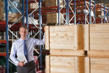 Photo: Portrait of confident businessman holding digital tablet and leaning on crates in warehouse Portrait of confident businessman holding digital tablet and leaning on crates in warehouse