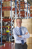 Photo: Portrait of smiling businessman with arms crossed in front of crates in warehouse Portrait of smiling businessman with arms crossed in front of crates in warehouse