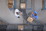 Photo: Businessman with digital tablet and worker packing box at conveyor belt in distribution warehouse Businessman with digital tablet and worker packing box at conveyor belt in distribution warehouse