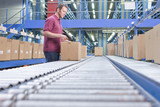 Photo: Worker with bar code reader scanning box on conveyor belt in distribution warehouse Worker with bar code reader scanning box on conveyor belt in distribution warehouse