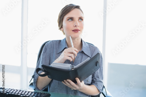 Photo: Thinking businesswoman holding her diary while sitting at her de Thinking businesswoman holding her diary while sitting at her de