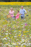 Foto: Portrait of smiling grandparents with granddaughter among wildflowers in sunny meadow Portrait of smiling grandparents with granddaughter among wildflowers in sunny meadow