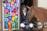 Photo : Girl in equestrian uniform feeding horse in doorway of trailer with rosettes covering door Girl in equestrian uniform feeding horse in doorway of trailer with rosettes covering door