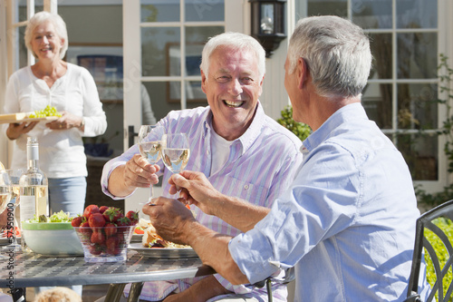 Photo: Smiling senior men drinking wine and enjoying lunch on sunny patio Smiling senior men drinking wine and enjoying lunch on sunny patio