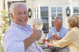 Photo: Portrait of smiling senior man drinking white wine on patio with friends in background Portrait of smiling senior man drinking white wine on patio with friends in background