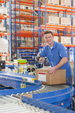 Photo: Portrait of smiling worker scanning cardboard box on production line in distribution warehouse Portrait of smiling worker scanning cardboard box on production line in distribution warehouse