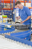 Photo: Worker examining machine parts in bin on production line in distribution warehouse Worker examining machine parts in bin on production line in distribution warehouse