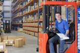 Photo: Portrait of smiling worker sitting in forklift with paperwork in distribution warehouse Portrait of smiling worker sitting in forklift with paperwork in distribution warehouse
