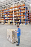 Photo: Worker with clipboard standing next to pallet of cardboard boxes in distribution warehouse Worker with clipboard standing next to pallet of cardboard boxes in distribution warehouse