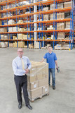 Photo: Portrait of smiling supervisor and worker leaning on pallet of cardboard boxes in distribution warehouse Portrait of smiling supervisor and worker leaning on pallet of cardboard boxes in distribution warehouse