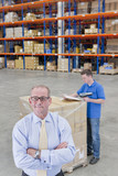 Photo : Portrait of confident supervisor with worker and pallet of cardboard boxes in distribution warehouse Portrait of confident supervisor with worker and pallet of cardboard boxes in distribution warehouse