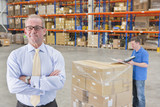 Photo: Portrait of confident supervisor with worker and pallet of cardboard boxes in distribution warehouse Portrait of confident supervisor with worker and pallet of cardboard boxes in distribution warehouse