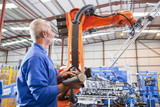 Photo: Worker controlling robotic machinery lifting steel fencing on production line in manufacturing plant Worker controlling robotic machinery lifting steel fencing on production line in manufacturing plant