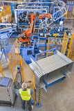 Photo: Worker controlling robotic machinery lifting steel fencing on production line in manufacturing plant Worker controlling robotic machinery lifting steel fencing on production line in manufacturing plant