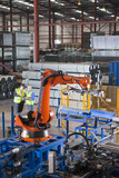 Photo: Businessman and worker controlling robotic machinery lifting steel fencing on production line in manufacturing plant Businessman and worker controlling robotic machinery lifting steel fencing on production line in manufacturing plant