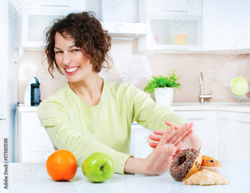 Photo: Dieting concept. Young Woman choosing between Fruits and Sweets Dieting concept. Young Woman choosing between Fruits and Sweets