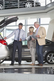 Photo: Salesman and couple with brochure looking into hatchback of car in car dealership showroom Salesman and couple with brochure looking into hatchback of car in car dealership showroom
