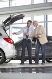 Photo: Salesman and customer with brochure looking into hatchback of car in car dealership showroom Salesman and customer with brochure looking into hatchback of car in car dealership showroom