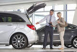 Photo: Salesman and customer with brochure looking into hatchback of car in car dealership showroom Salesman and customer with brochure looking into hatchback of car in car dealership showroom