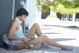 Photo: Young man with backpack, coffee cup and headphones using digital tablet on sidewalk Young man with backpack, coffee cup and headphones using digital tablet on sidewalk