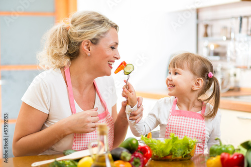 Photo: kid daughter feeding mother vegetables in kitchen kid daughter feeding mother vegetables in kitchen