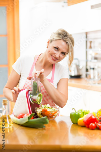 Photo: Cute woman cutting vegetables with device at the kitchen table Cute woman cutting vegetables with device at the kitchen table