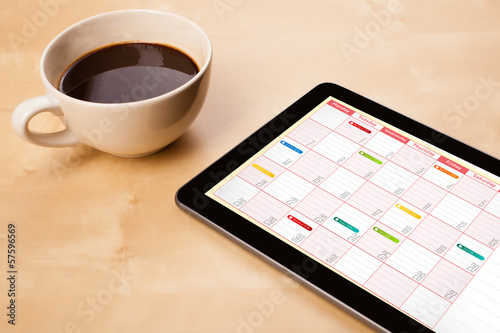 Photo: Tablet pc showing calendar on screen with a cup of coffee on a d Tablet pc showing calendar on screen with a cup of coffee on a d