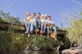 Photo: Portrait of smiling multi-generation family sitting barefoot on footbridge over stream Portrait of smiling multi-generation family sitting barefoot on footbridge over stream