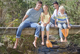 Photo: Portrait of smiling family with fishing nets sitting barefoot on footbridge over stream Portrait of smiling family with fishing nets sitting barefoot on footbridge over stream