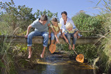 Photo: Family with fishing nets sitting barefoot on footbridge and looking down at stream Family with fishing nets sitting barefoot on footbridge and looking down at stream