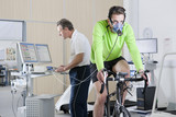 Photo: Sports scientist at computer and cyclist with mask on exercise bike in laboratory Sports scientist at computer and cyclist with mask on exercise bike in laboratory