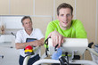Photo: Portrait of runner holding mask and leaning on treadmill in laboratory with sports scientist in background Portrait of runner holding mask and leaning on treadmill in laboratory with sports scientist in background