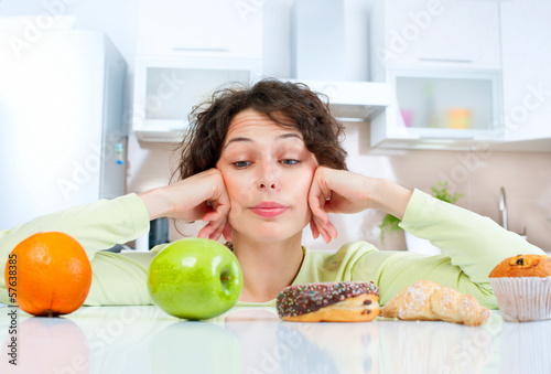 Photo: Dieting concept. Young Woman choosing between Fruits and Sweets Dieting concept. Young Woman choosing between Fruits and Sweets