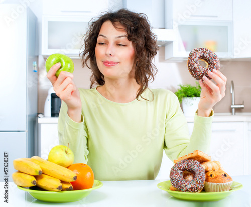 Photo: Dieting concept. Young Woman choosing between Fruits and Sweets Dieting concept. Young Woman choosing between Fruits and Sweets