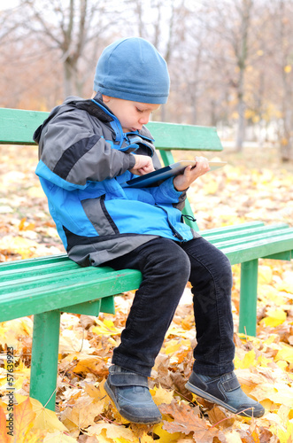 Photo: Little boy reading a tablet computer in park Little boy reading a tablet computer in park