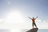 Photo: Male rock climber standing with arms outstretched on top of rock overlooking ocean Male rock climber standing with arms outstretched on top of rock overlooking ocean