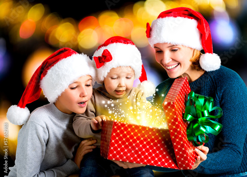Photo: Mother with children opens the box with gifts on the christmas h Mother with children opens the box with gifts on the christmas h