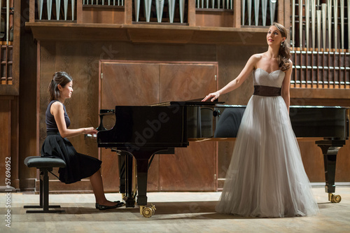 Photo: Woman pianist plays piano and singer stands next Woman pianist plays piano and singer stands next