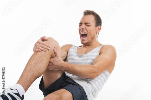 Photo: Man screaming from a pain in his knee. While isolated on white Man screaming from a pain in his knee. While isolated on white