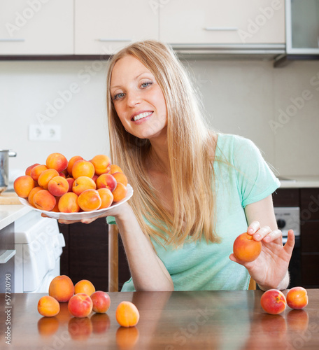 Photo: young blonde housewife with heap of apricots t domestic kitchen young blonde housewife with heap of apricots t domestic kitchen